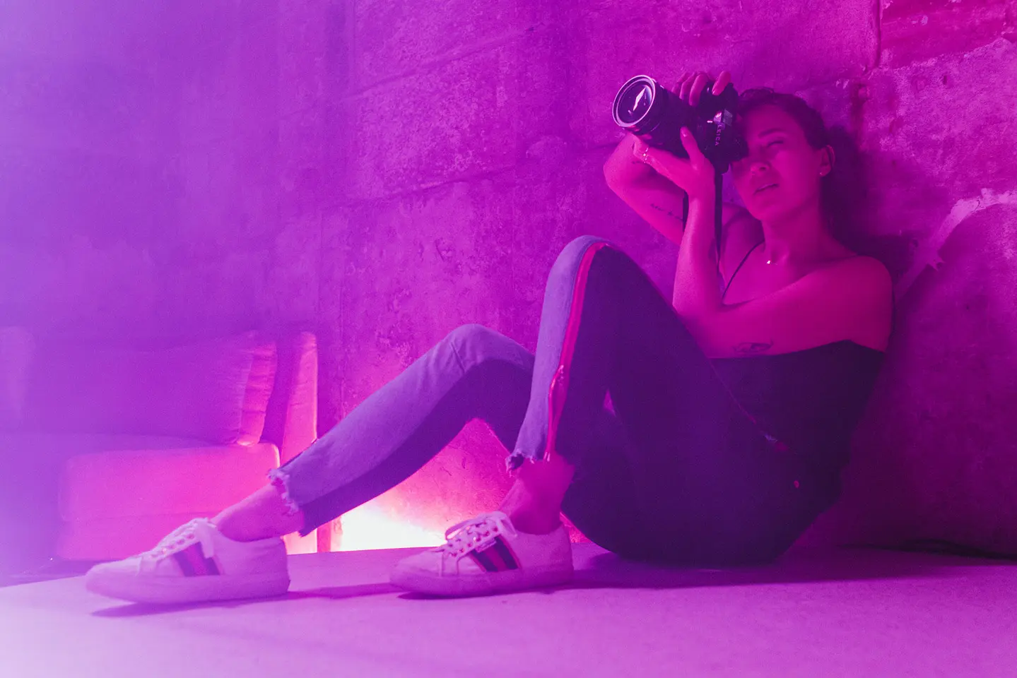 Alex Drewniak sits on the floor, taking pictures in a room lit by pink-purple light.