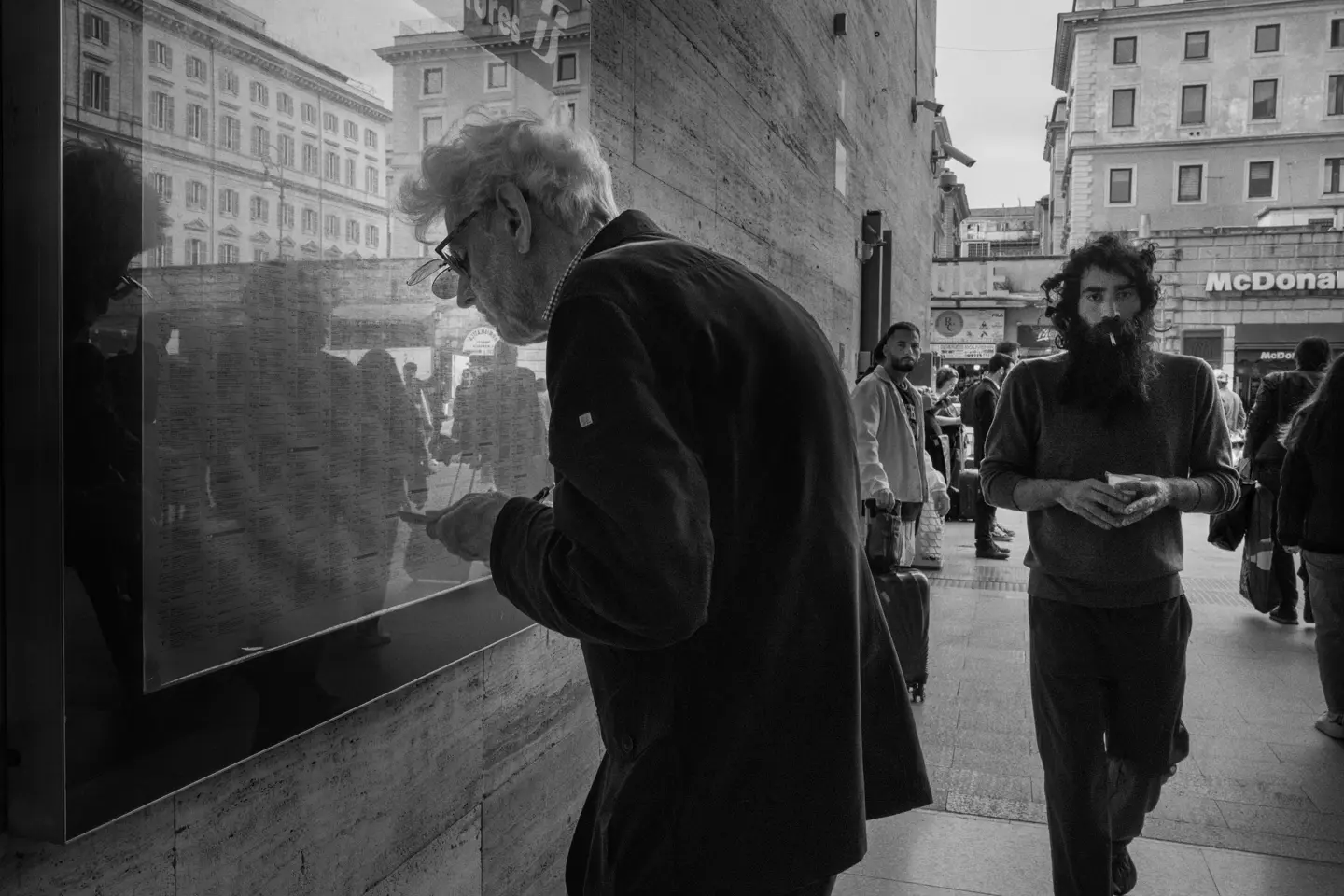 Elderly man in the city looking at a train timetable behind a pane of glass.