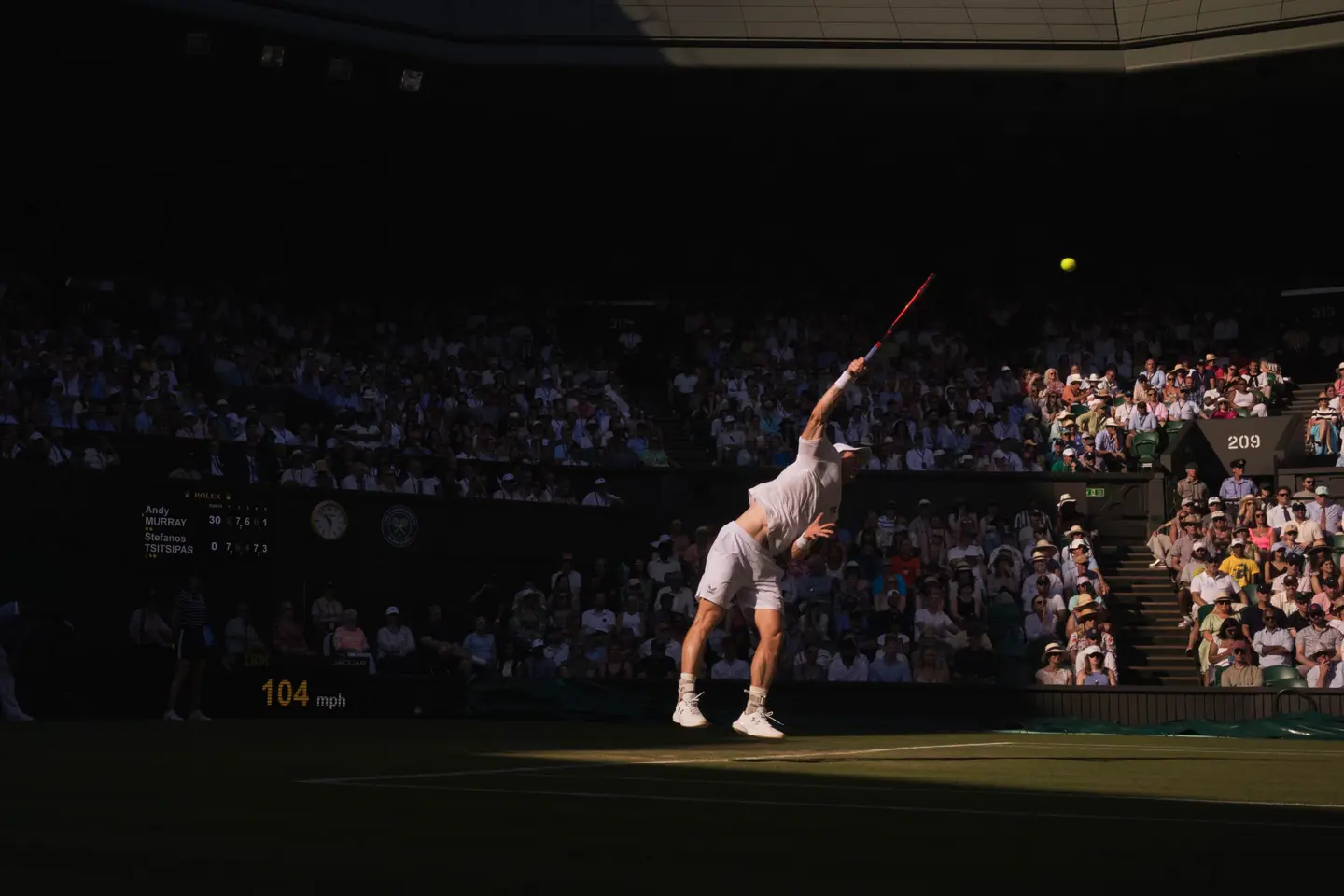 Tennis player serving during a match, with a crowd watching from the stands.