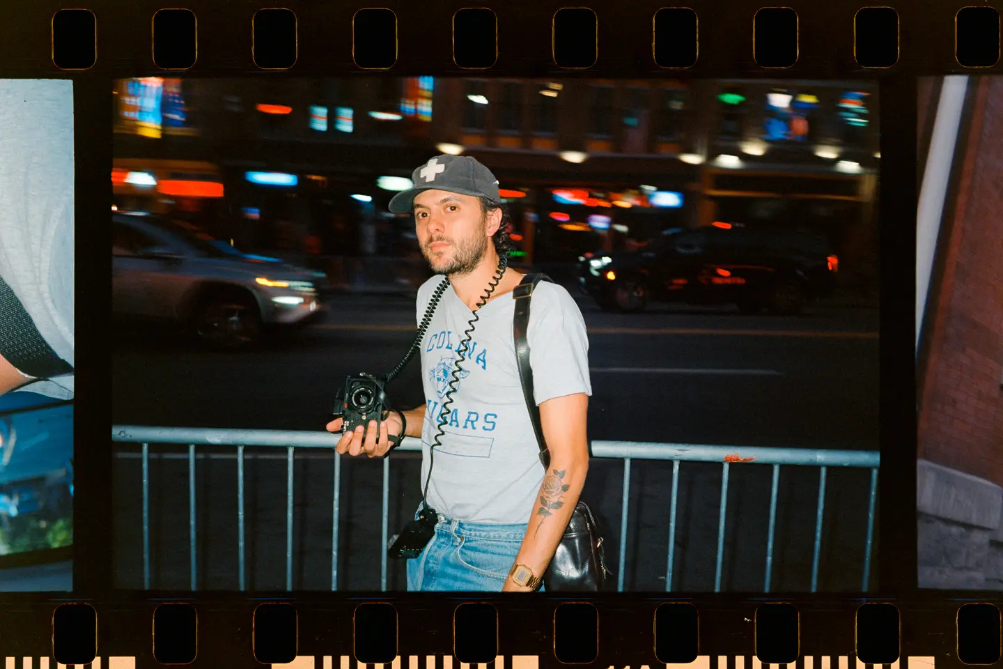 Joe Greer with a Leica M6 in his hand standing at a street at night.
