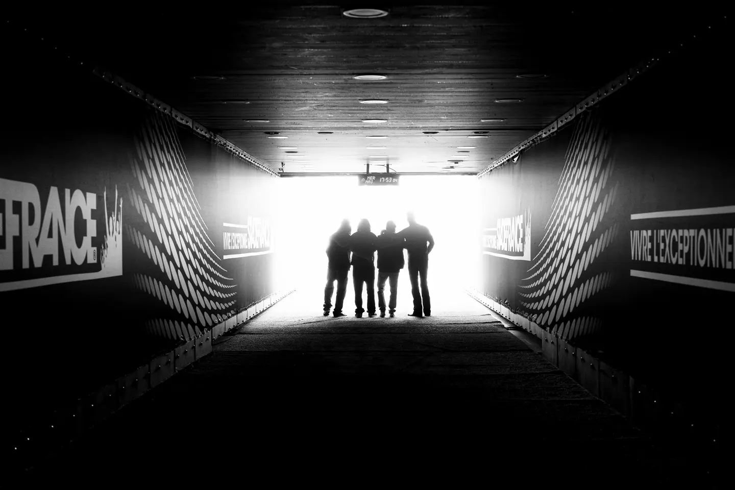 Four people are standing in a stadium tunnel with the sign "Stade France" in the light at the end of the corridor.