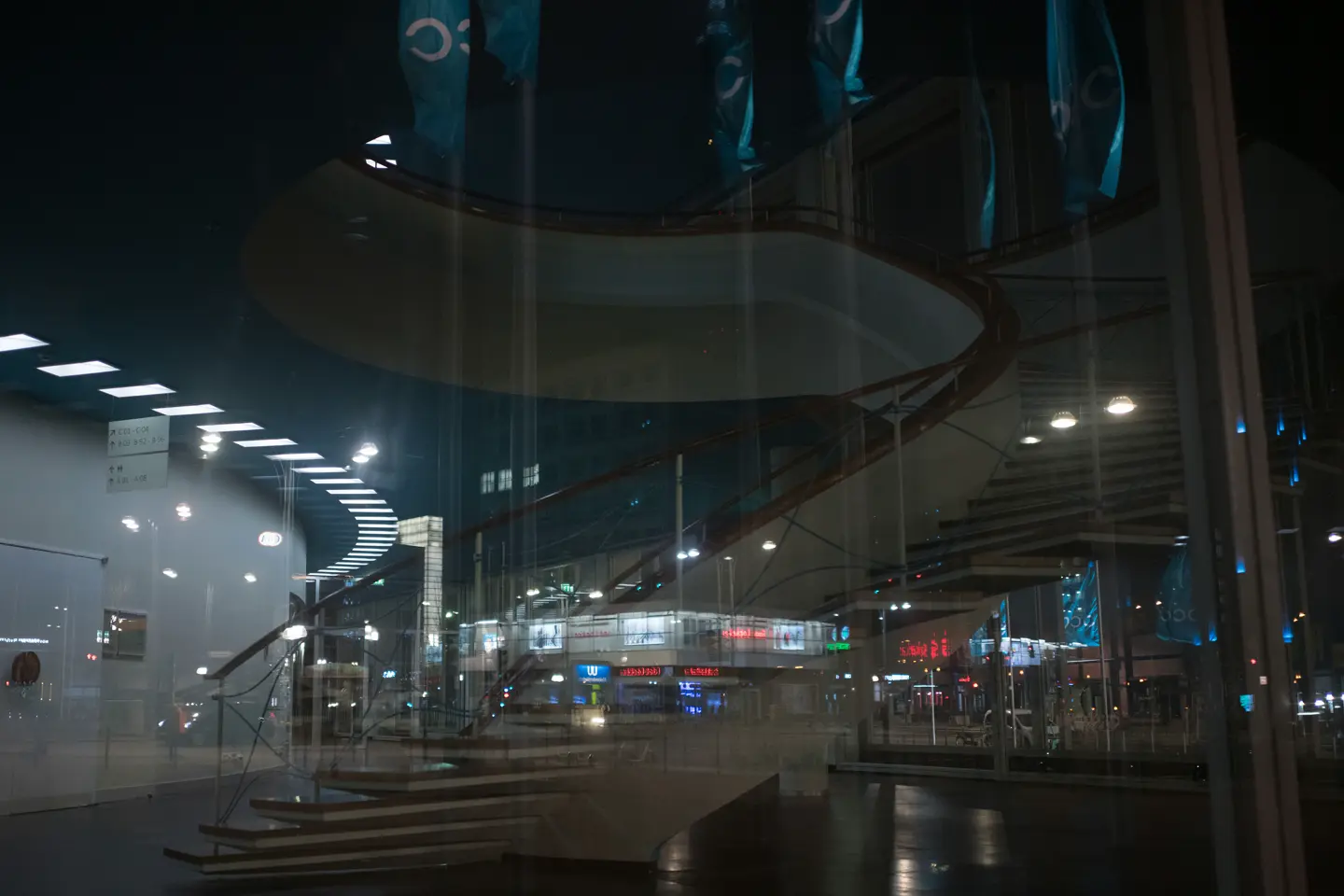 Reflection of a spiral staircase and a city at night in the glass front of a building.