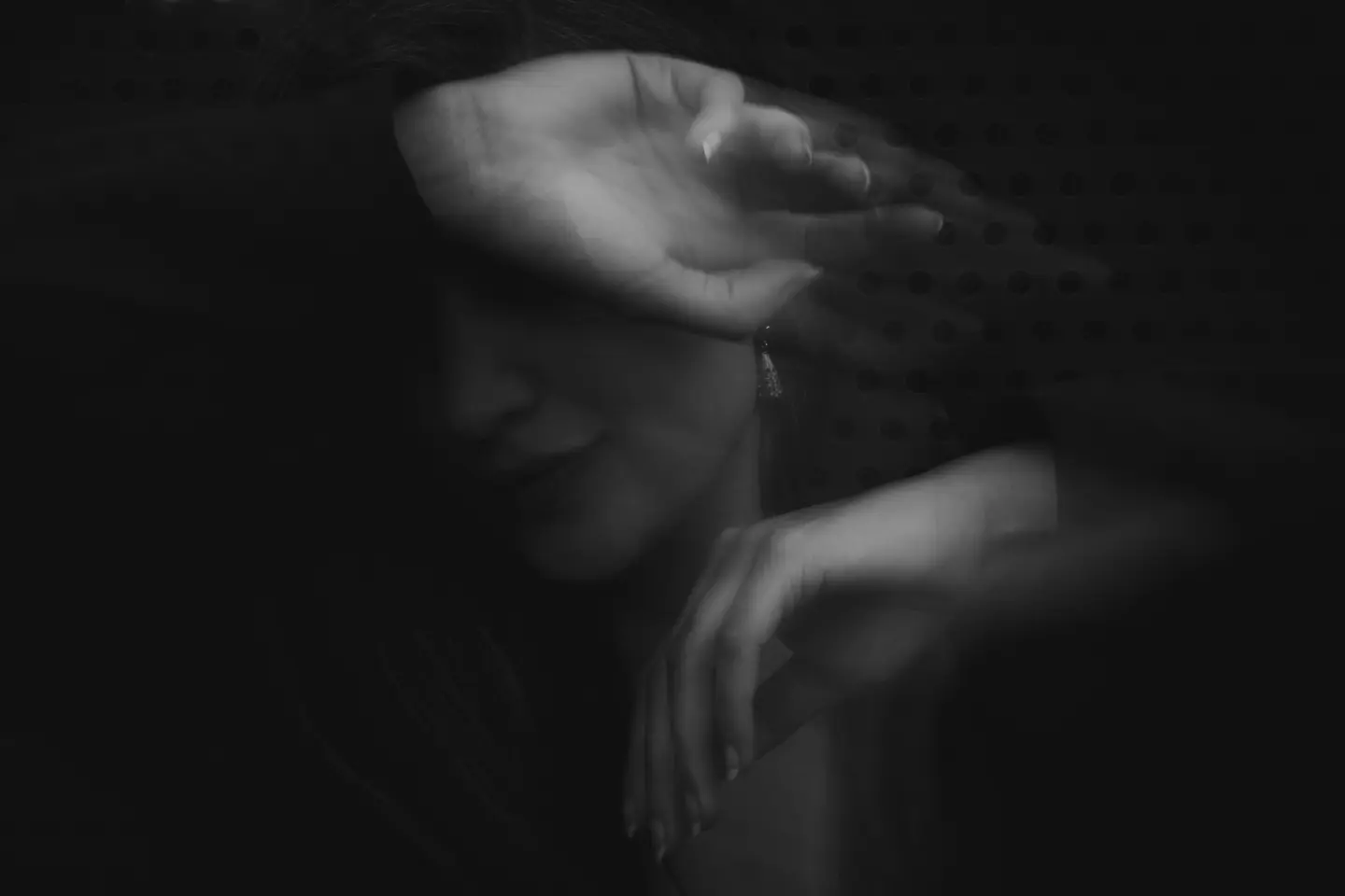 Blurred black and white image of a person covering her face with her arm.