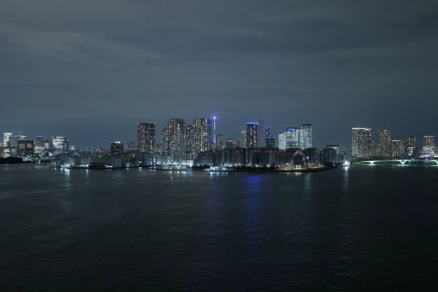 Illuminated skyline of Tokyo at night, with a view of the water in the foreground.