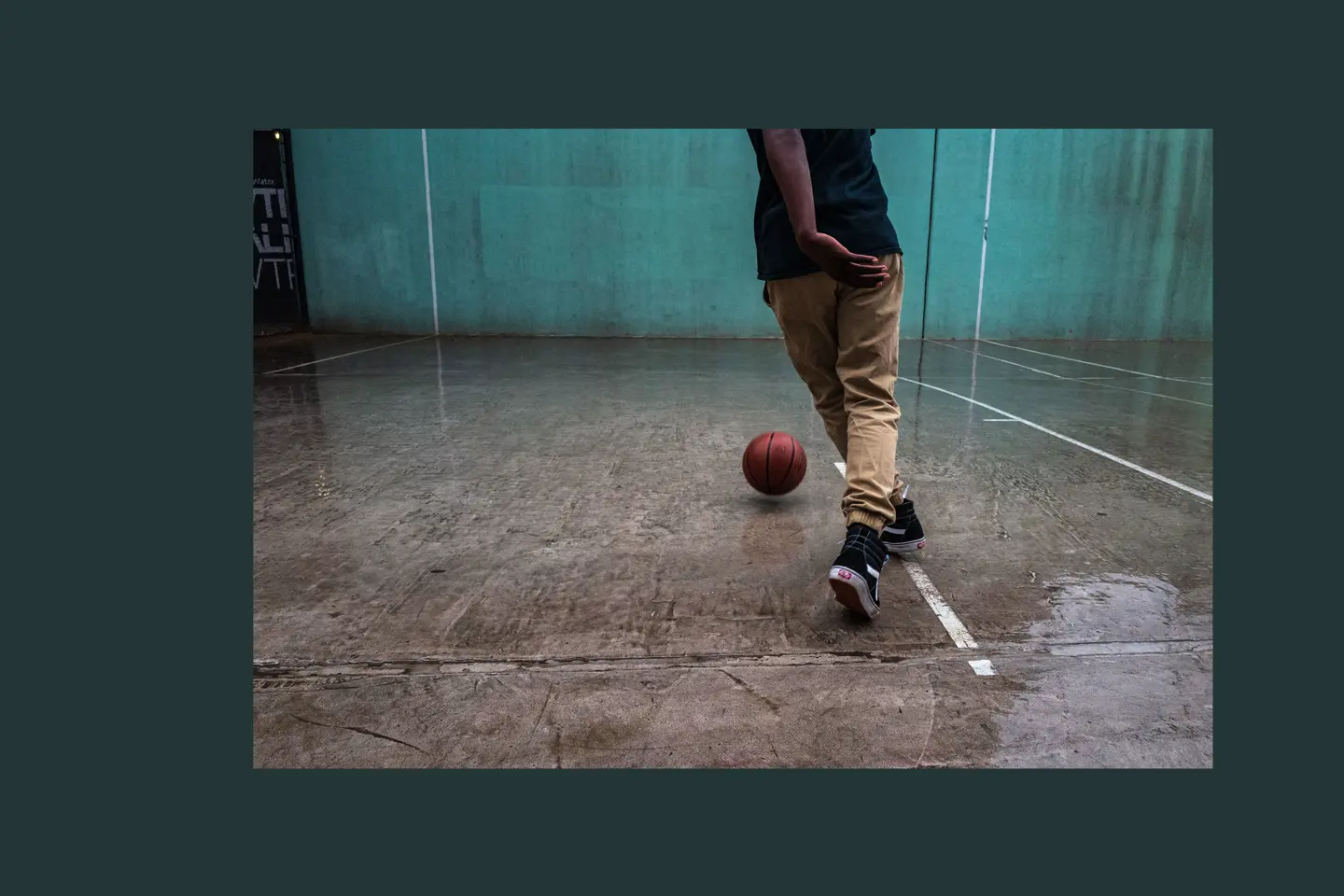 Person playing basketball on a wet court with a turquoise wall in the background.