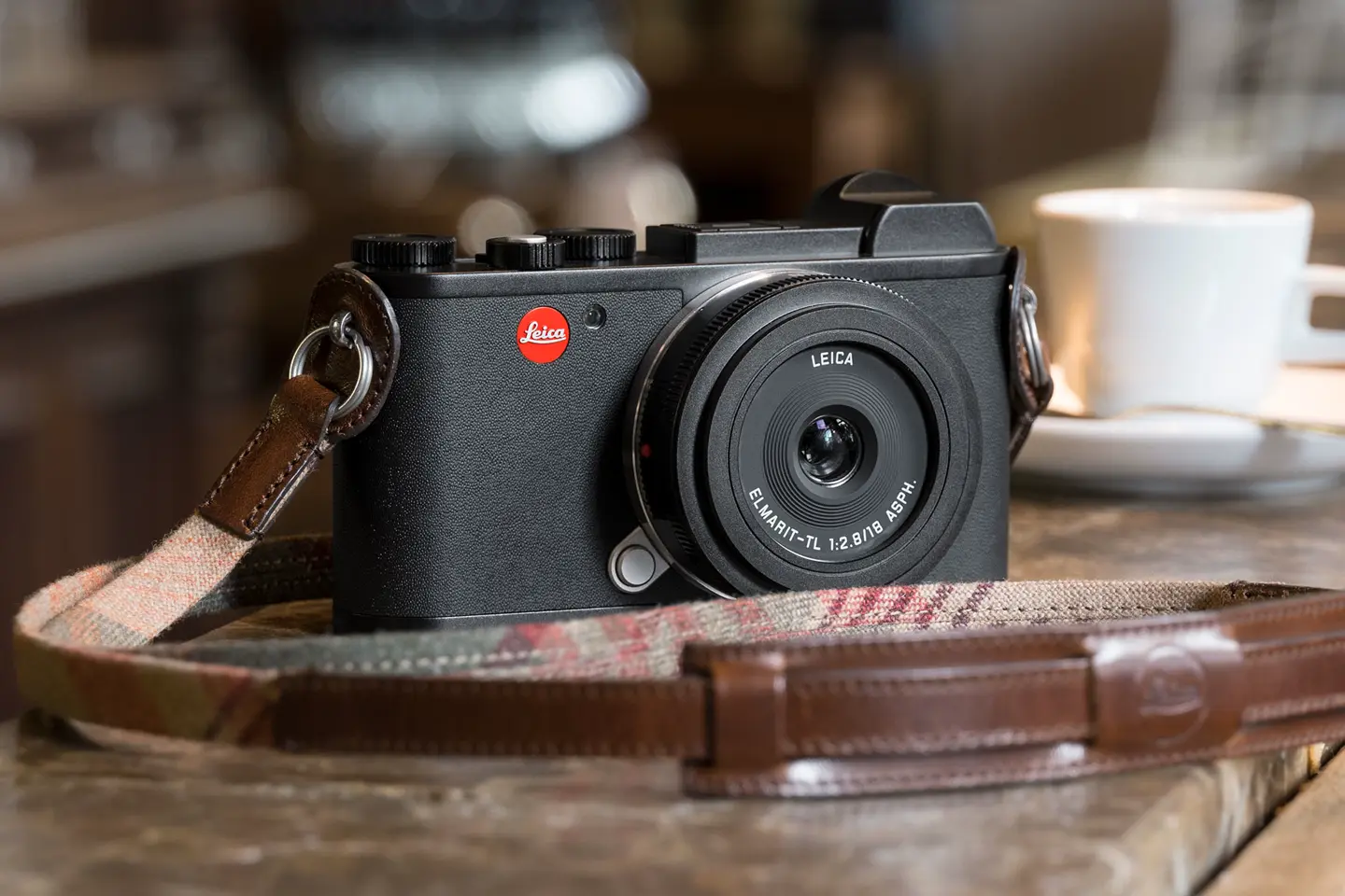 Leica camera on wooden counter with coffee cup in background