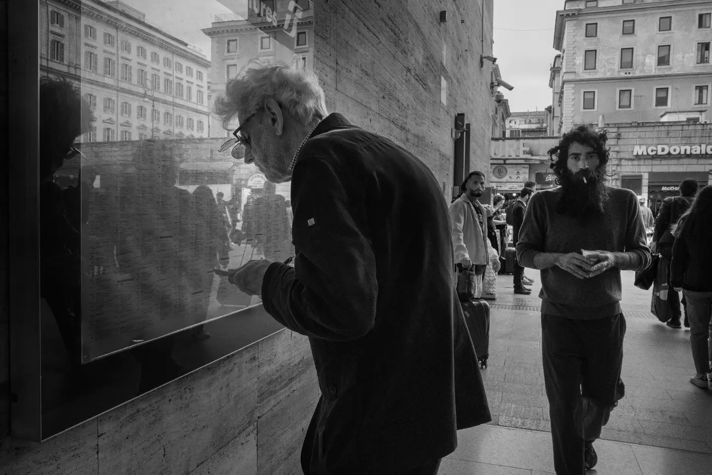 Elderly man in the city looking at a train timetable behind a pane of glass.