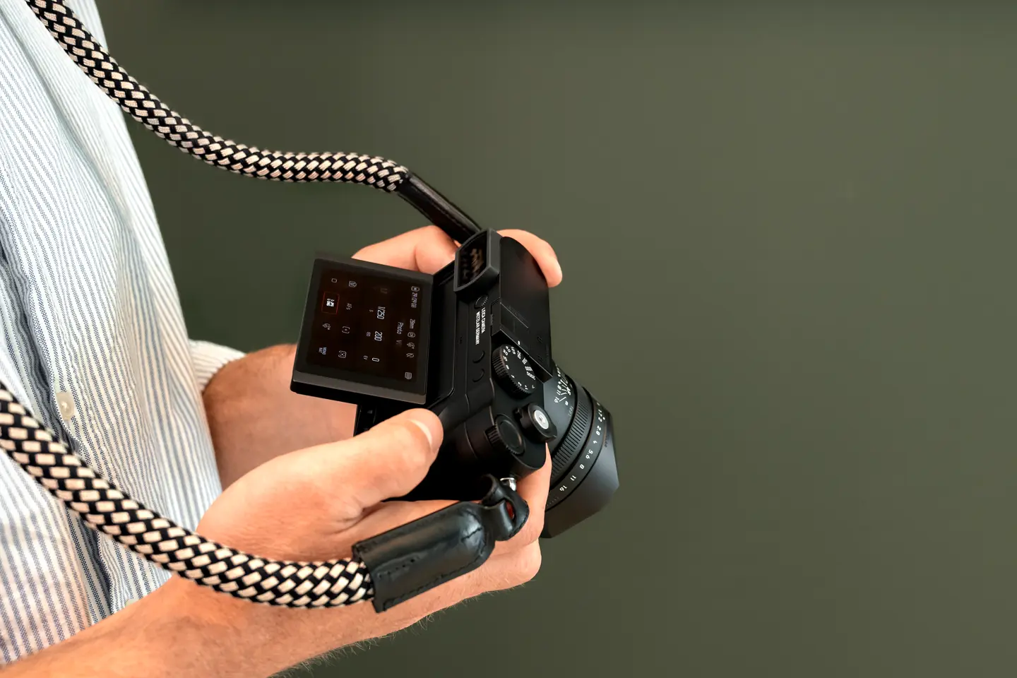 Man holding a leica Q3 Monochrom in front of a green background