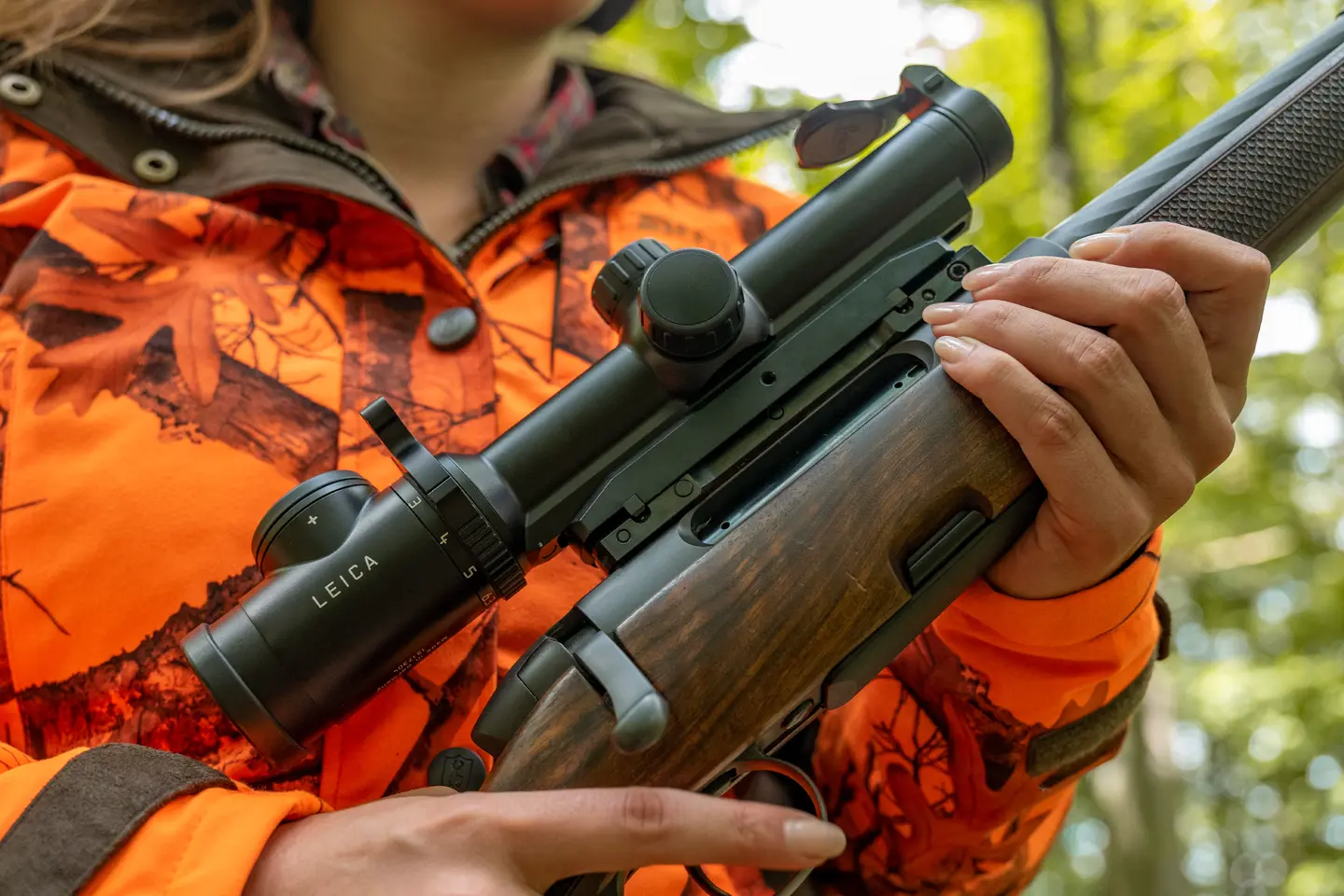 female-hunter-driven-hunt-attire-holding-hunting-rifle-with-leica-magnus-riflescope-in-forest