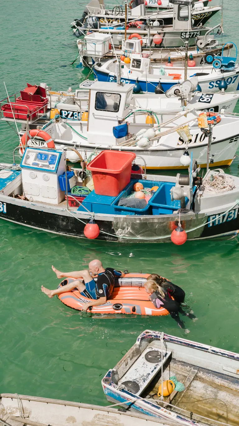Colour image of a row of boats and a man and 2 kids on an orange inflatable boat.