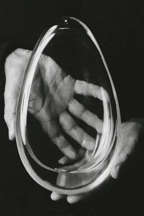 Deux mains en noir et blanc qui tiennent un objet transparent 