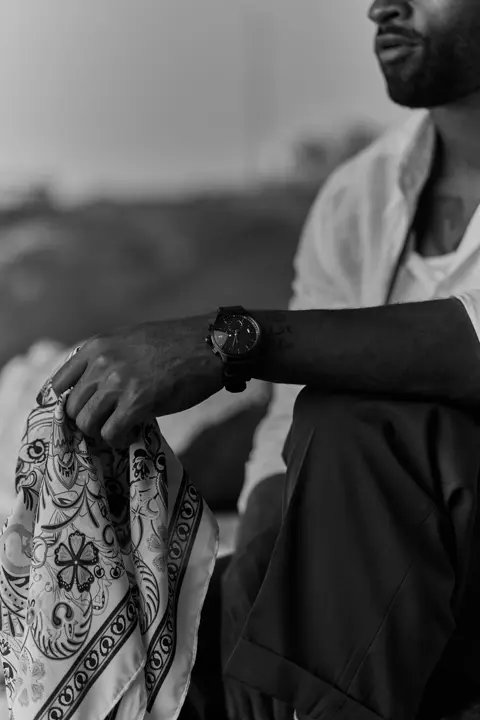 Black-and-white photograph, man sitting on a rock holding a cloth in his hand.
