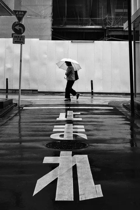 A woman walks across a street with an umbrella