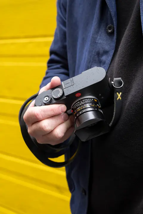 Jesse with a Leica in front of a yellow wall