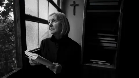 black-and-white photograph, an elderly woman holding a book looks thoughtfully out of the window
