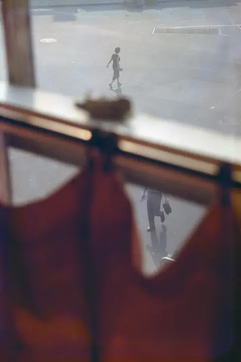 Blich durch roten Vorhang auf die Straße laufende Menschen, Saul Leiter
