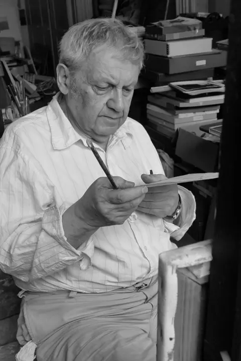 Saul Leiter sitting at home in New York holding a paint brush