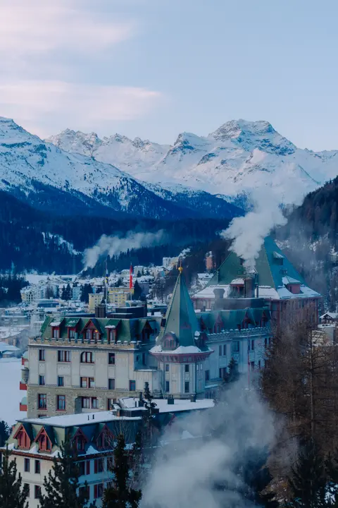 Historic alpine hotel surrounded by snowy peaks and winter mist.