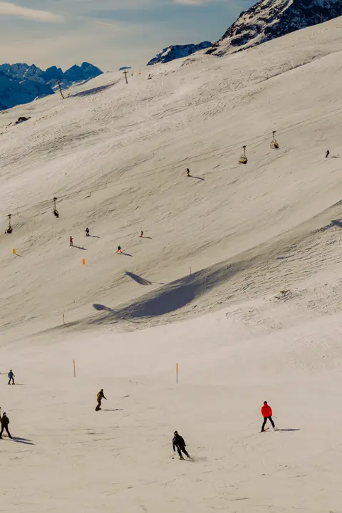 Skiers descending a wide snow-covered slope in the mountains.