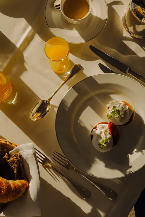 Sunlit breakfast table with poached eggs, pastries, coffee, and orange juice.
