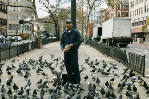 Street portrait of Jason Roman surrounded by pigeons in an urban setting, capturing everyday city life, human interaction, and spontaneous moments in New York.