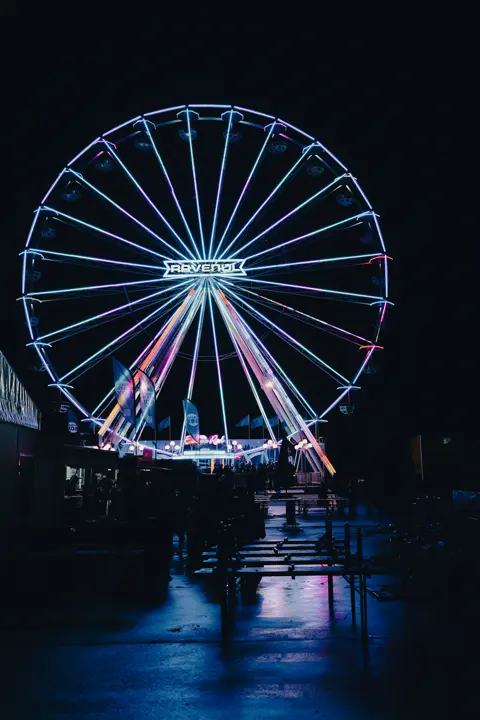 Illuminated Ferris wheel at a motorsport event, creating a vibrant nighttime atmosphere at the race circuit.