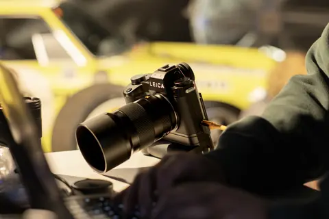 Leica camera connected to a workstation beside a classic race car, highlighting digital workflow in automotive photography.