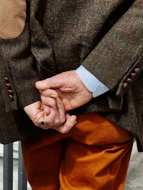 Close-up of folded hands and tailored clothing, capturing subtle details, texture, and everyday human presence in street photography.
