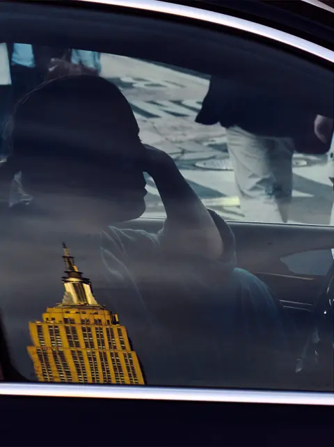 Reflection of a city skyline and a passenger inside a car window, capturing layered urban storytelling and street photography.