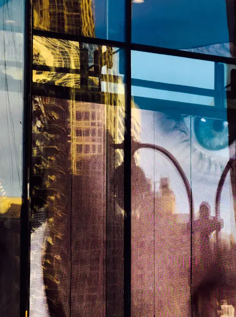 Architectural reflections and digital imagery merge on a glass façade, creating an abstract urban photography composition.