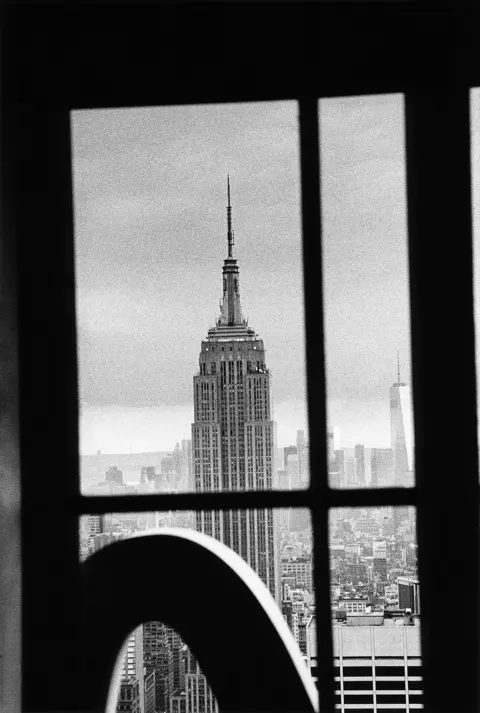 Schwarzweißes analoges Foto des Empire State Buildings, durch einen Fensterrahmen gesehen.
