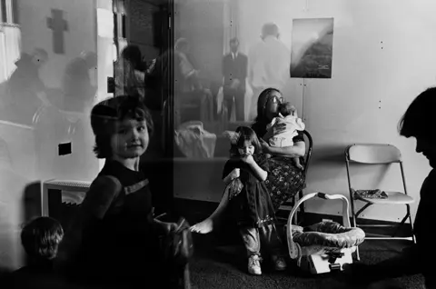 Black-and-white documentary photograph of families gathered inside a small rural church in Montana, capturing community life and everyday moments along Highway 93.
