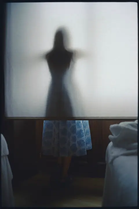 Silhouette of a woman behind a translucent screen, creating an abstract portrait with soft light, shadow and an intimate analog mood.