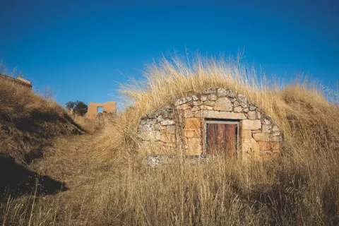 Abandoned stone structure overgrown with dry grass in rural Spain, reflecting isolation, decay and depopulation in España Vacía.