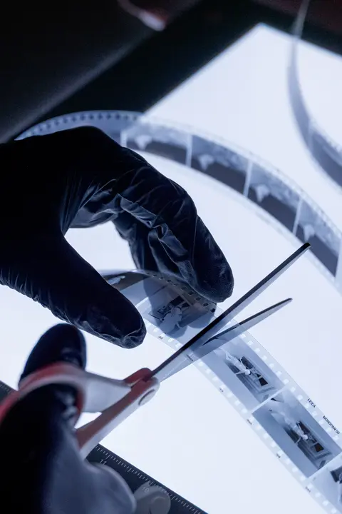 Gloved hands cutting black-and-white film negatives on a light table.