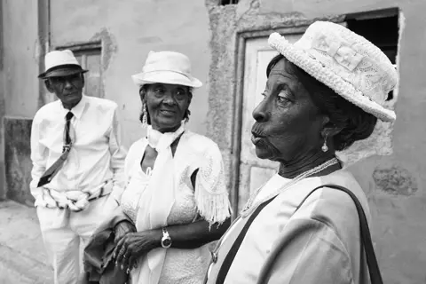 Black-and-white portrait of three elegantly dressed older adults in Cuba, capturing style, character and everyday social life.