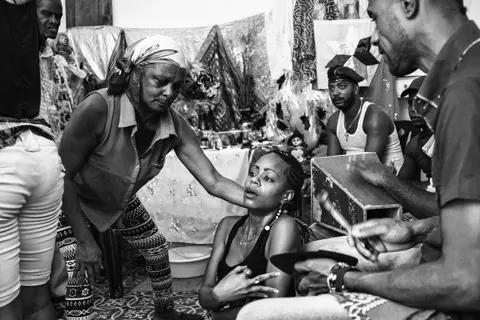 Black-and-white documentary photograph of a Santería ceremony in Cuba, showing participants gathered in an intimate ritual setting.