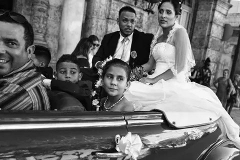 Black-and-white photograph of a Cuban wedding party riding in a vintage convertible, capturing celebration, family and everyday culture.