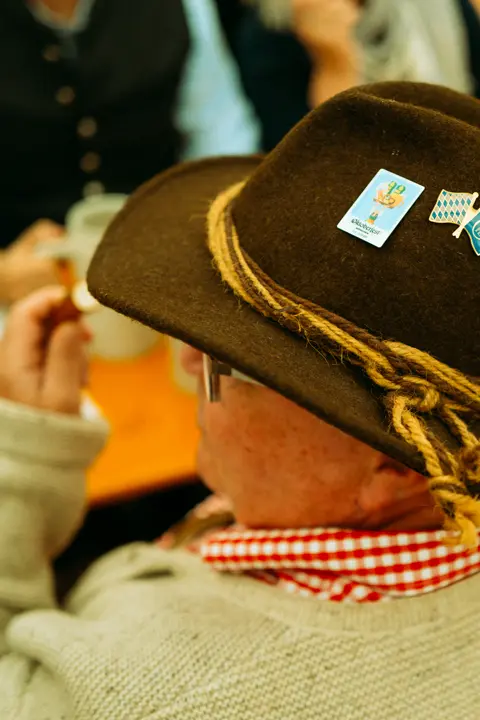 Close-up of a traditional Bavarian hat decorated with Oktoberfest pins inside a Munich beer tent, highlighting local customs and festival culture.