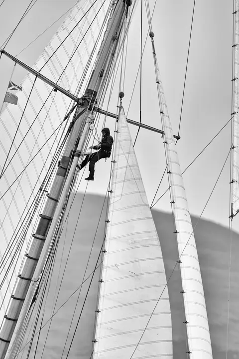 Homme dans les hauteurs des voiles d'un bateau