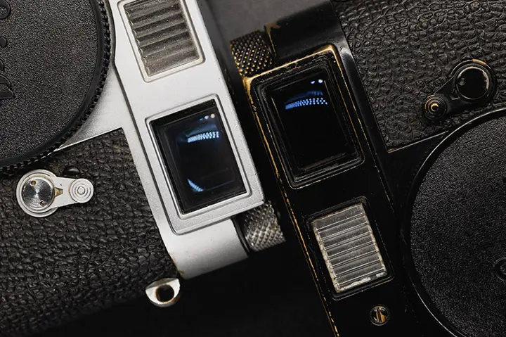 A silver and Black vintage cameras showing their rangefinder.