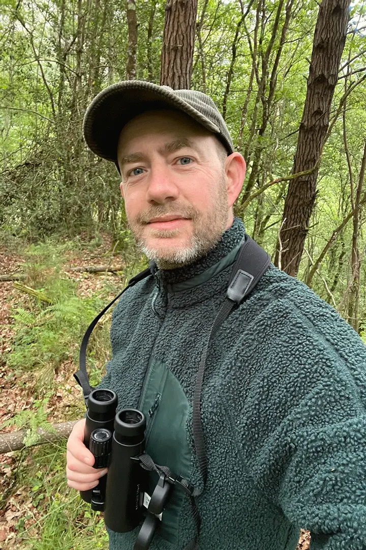 A portrait of Will Rose with a pair of Leica binoculars. 
