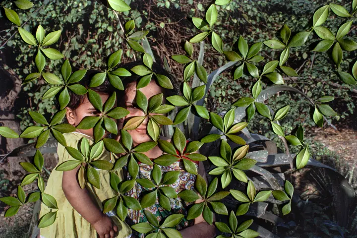 Woman with baby in arms stands behind leaves