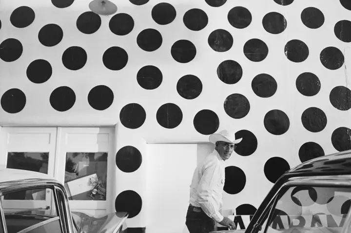 Man with hat in front of a white wall with large black dots