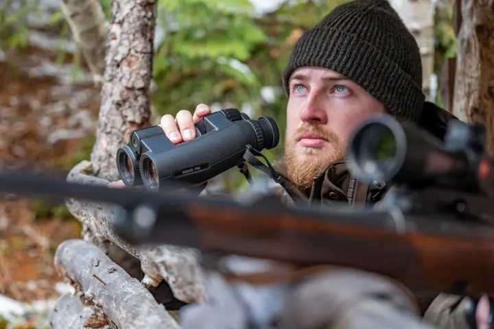 Hunter is sitting on a high seat and looking through his Leica Geovid Pro