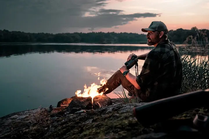 Hunter is sitting in front of an open fire and using his Leica Geovid R 8x42
