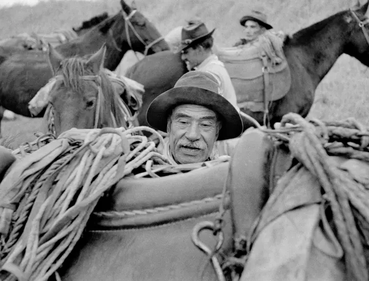 Black and White Image of a man with a hat, about to get on a horse