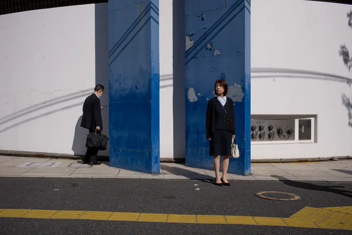 A smartly dressed woman stands waiting at the side of the road.
