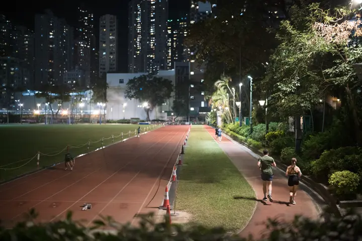 A man and a woman jogging on the running track in the stadium at night under floodlights.