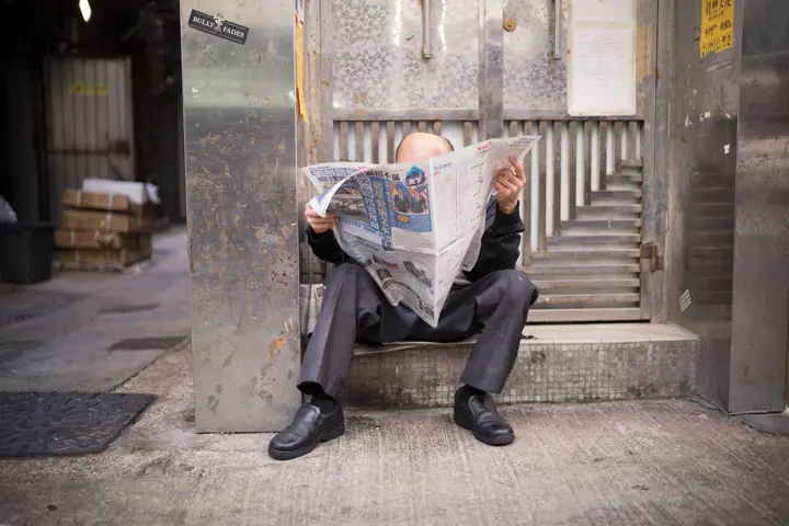 Old man reading newspaper sitting on stairs